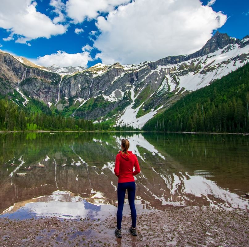 Woman standing in front of lake looking at glacier national park