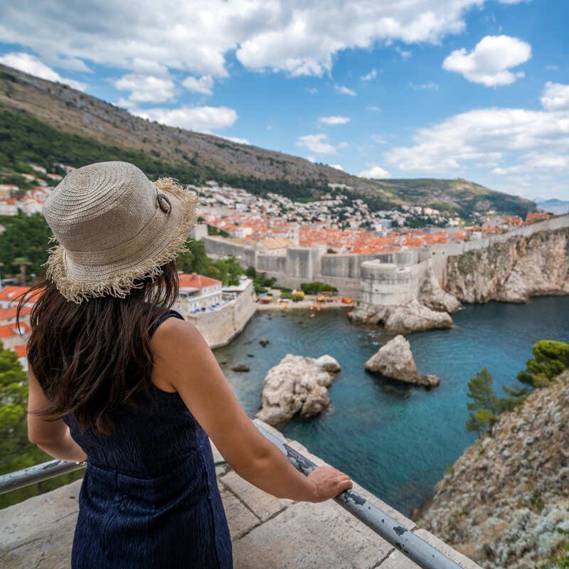 Young Female Tourist Gazing At The Medieval Citadel Of Dubrovnik, Croatia, Adriatic Coast