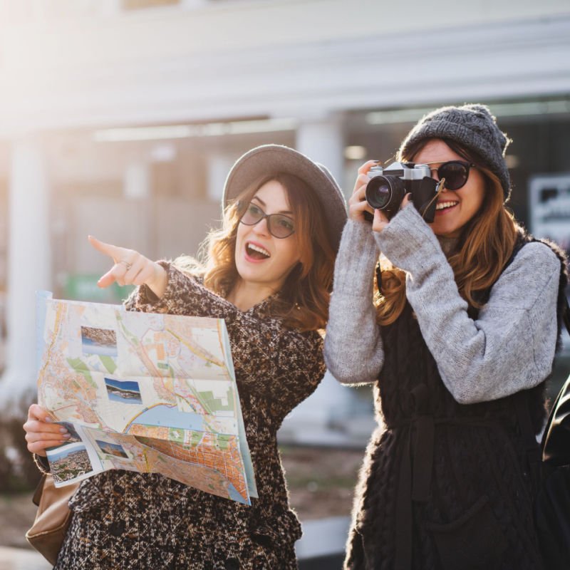 Young joyful women expressing positivity, using map, vacation with bags, camera, making photo, cheerful emotions, great mood