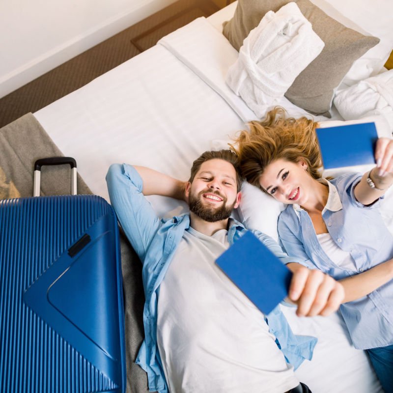 Couple lying on bed holding up passports