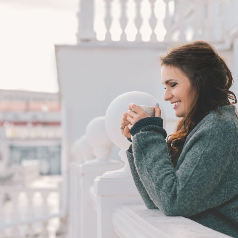 Beautiful smiling woman relaxing and drinking coffee on the balcony in the morning