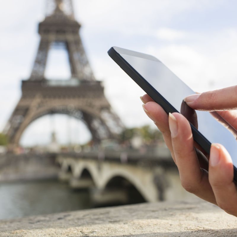 Woman in Paris using her cell phone in front of Eiffel Tower, seine bridge background, message sms e-mail