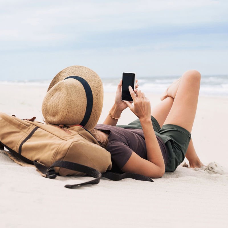 Young woman lying with smart phone on a beach. Girl looking at mobile phone.