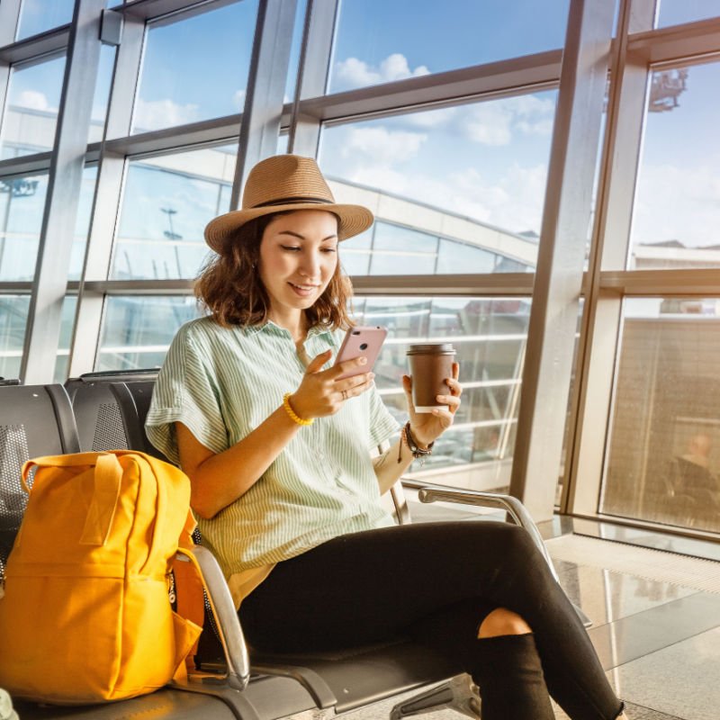 Asian girl waiting for departure at the airport on your vacation. Uses a smartphone and drinks coffee