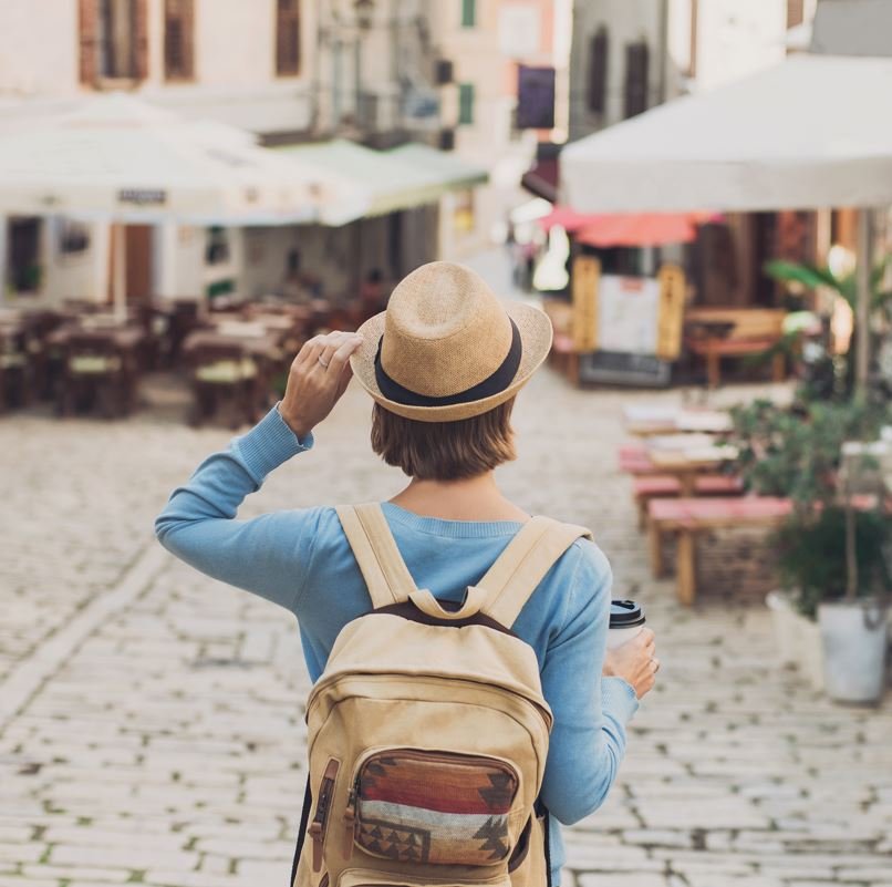 Solo Female traveler holding her hat and a cup of coffee while looking down a street in europe