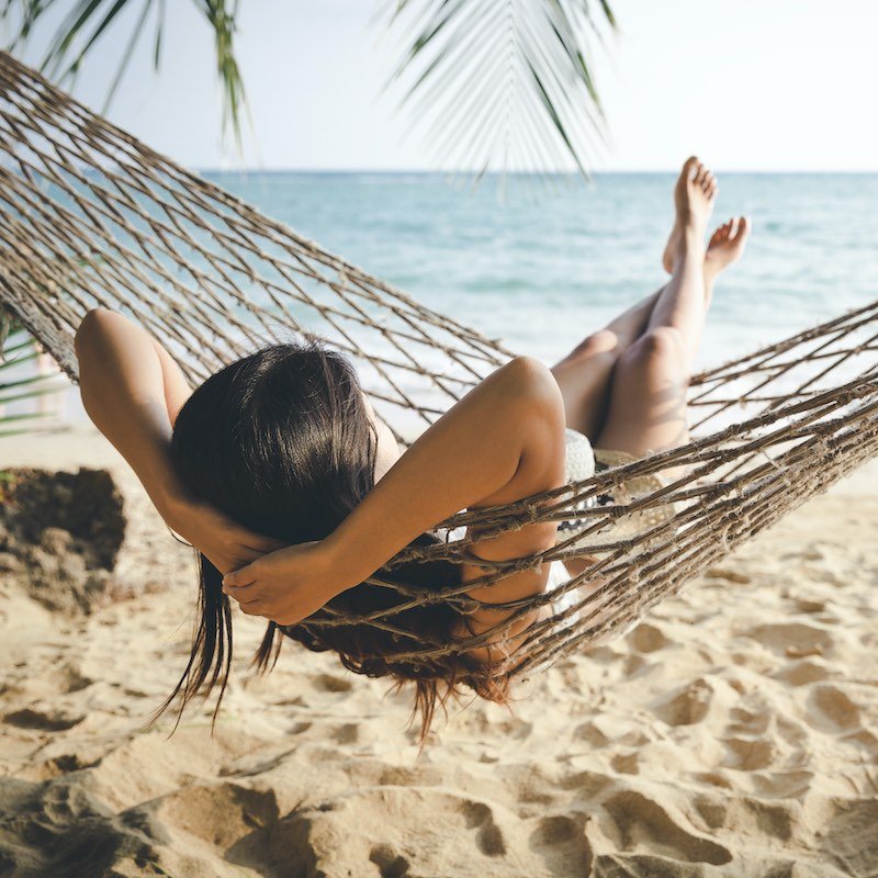 Woman Relaxing In Hammock In Front Of A Tropical Beach, Unspecified Location