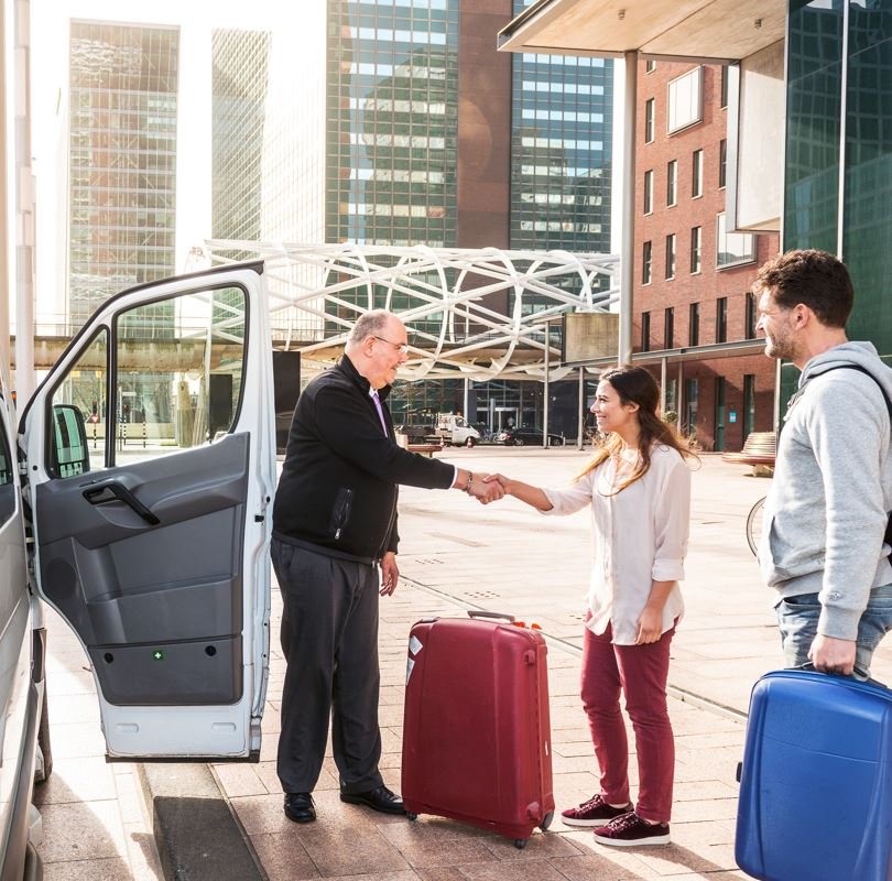 Travelers giving luggage to an airport shuttle driver