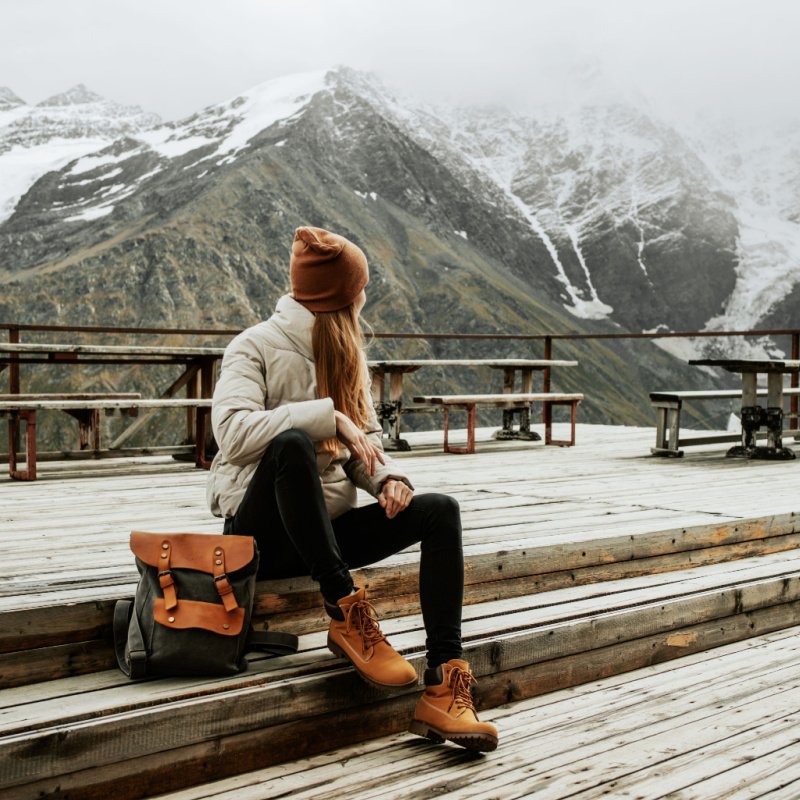 a woman sits on a wooden deck and looks at the snow capped mountains in the distance