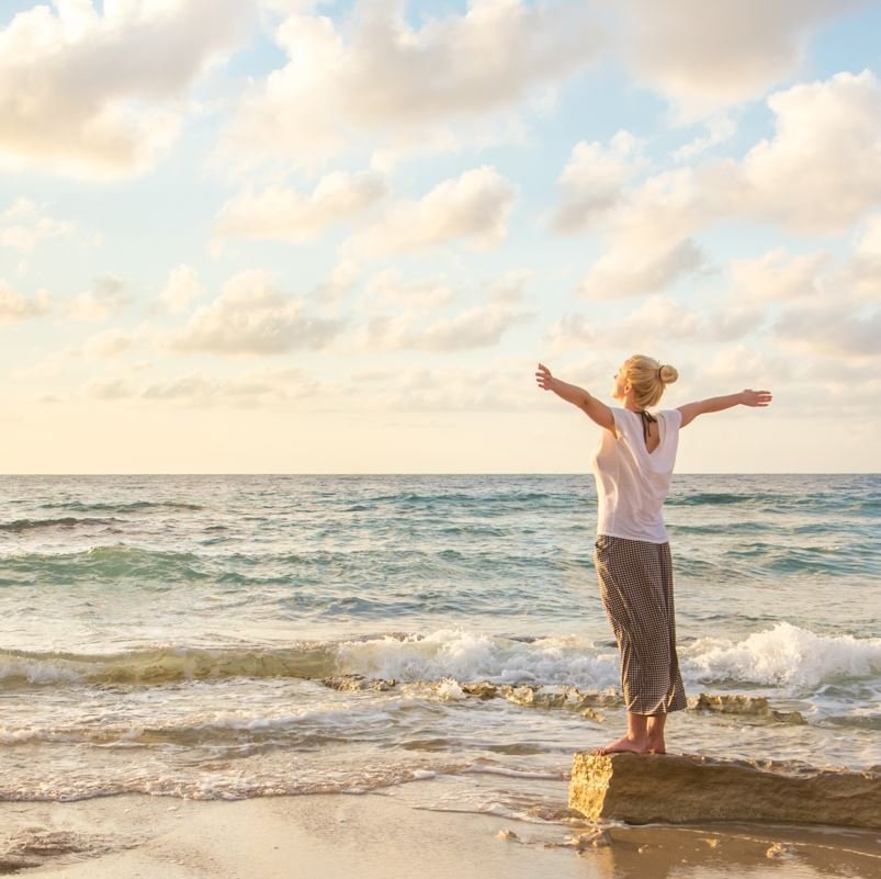 Woman on beach facing sun, wellness