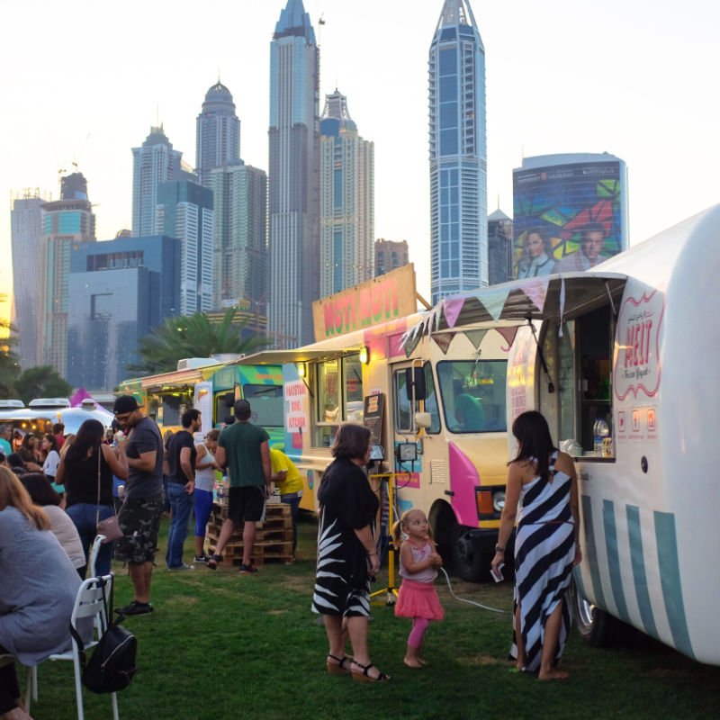 Dubai, UAE People lounging near food trucks at the Food Truck Jam, a weekend event with food trucks and live music at the Emirates Golf Club. Dubai Media City in the backdrop.