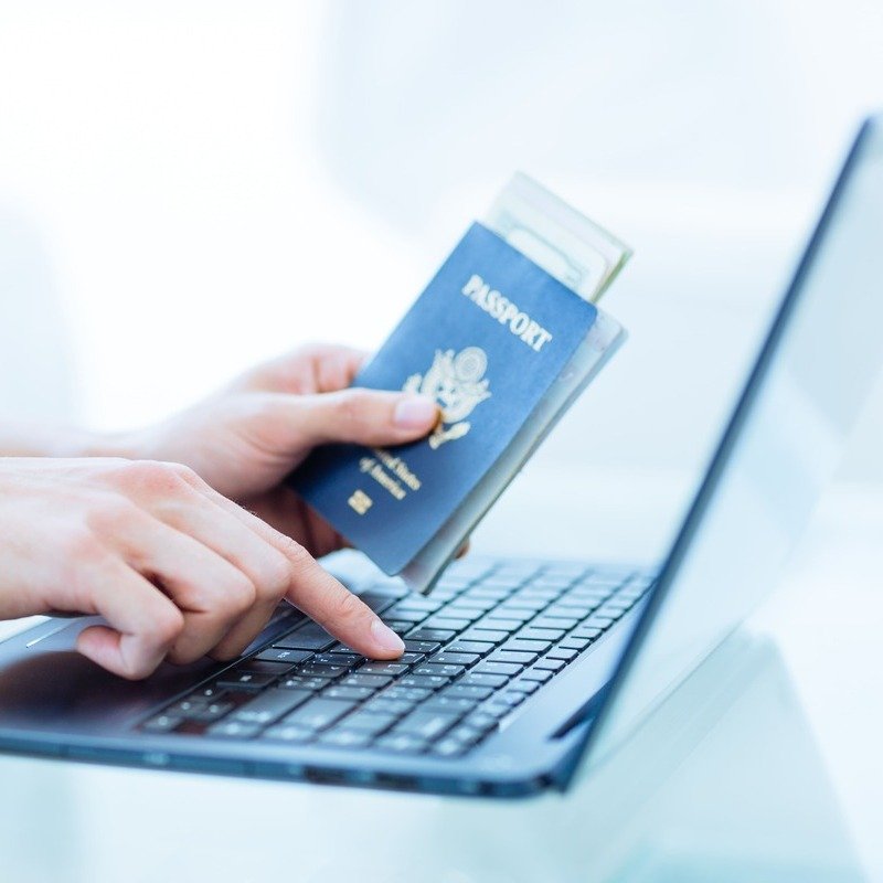 A Woman Holding Up A Passport As She Types On Her Computer, digital nomad concept