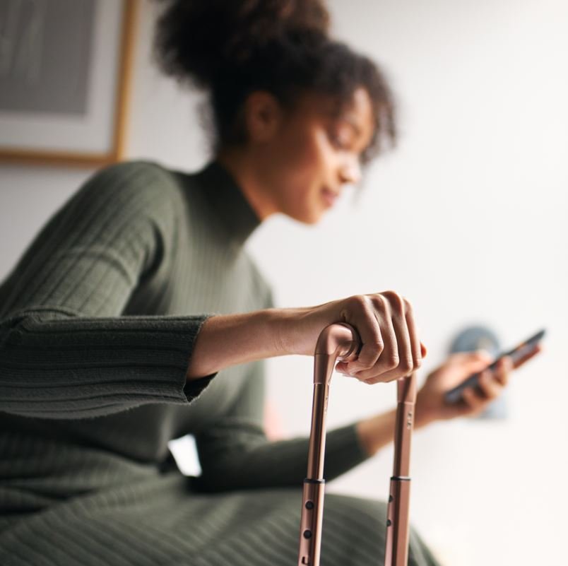 Woman looking at her phone while resting hand on suitcase