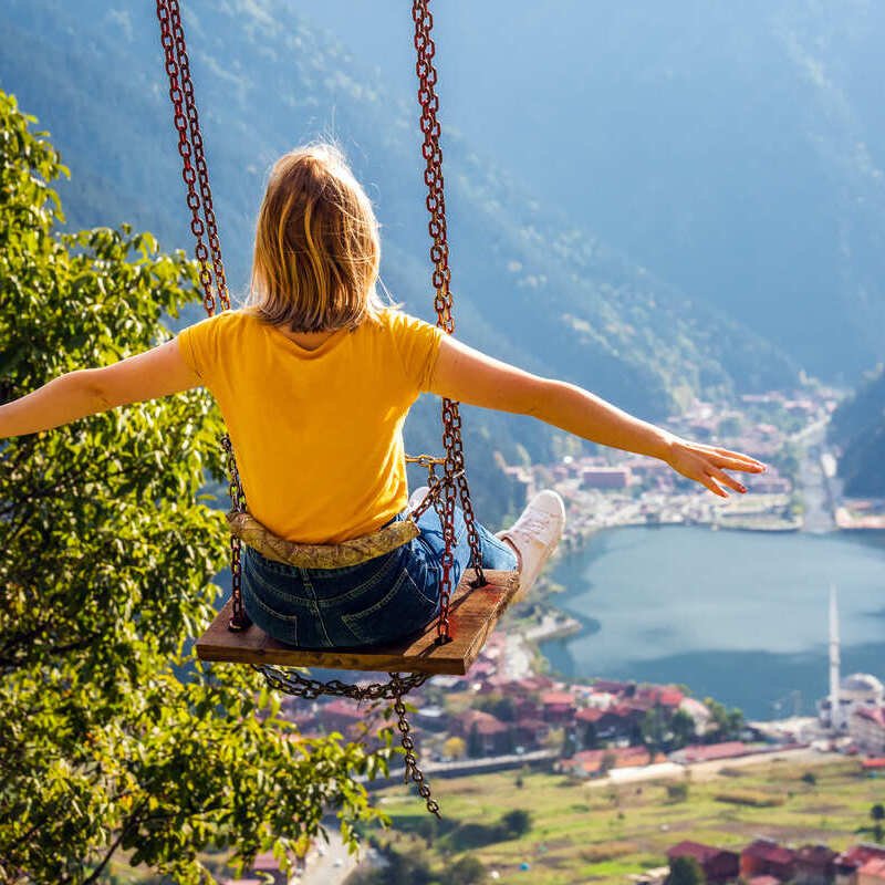 Young Woman Seen From Behind As She Goes On A Swing With Her Arms Open Facing The Historical City Of Trabzon, Nestled Between The Black Sea And The Pontic Alps In Turkyie, Turkey