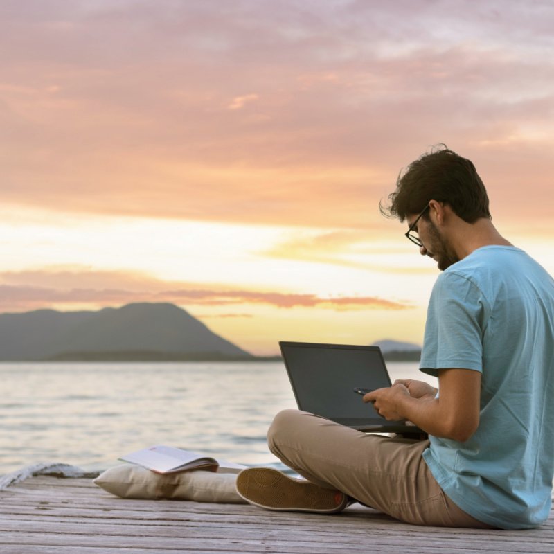 man on dock in sunset with laptop
