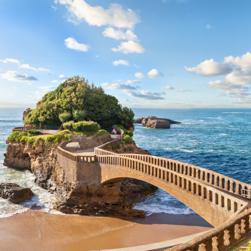 A bridge to a small island near coast in Biarritz, France. The island is tiny with the ocean almost taking it all. 
