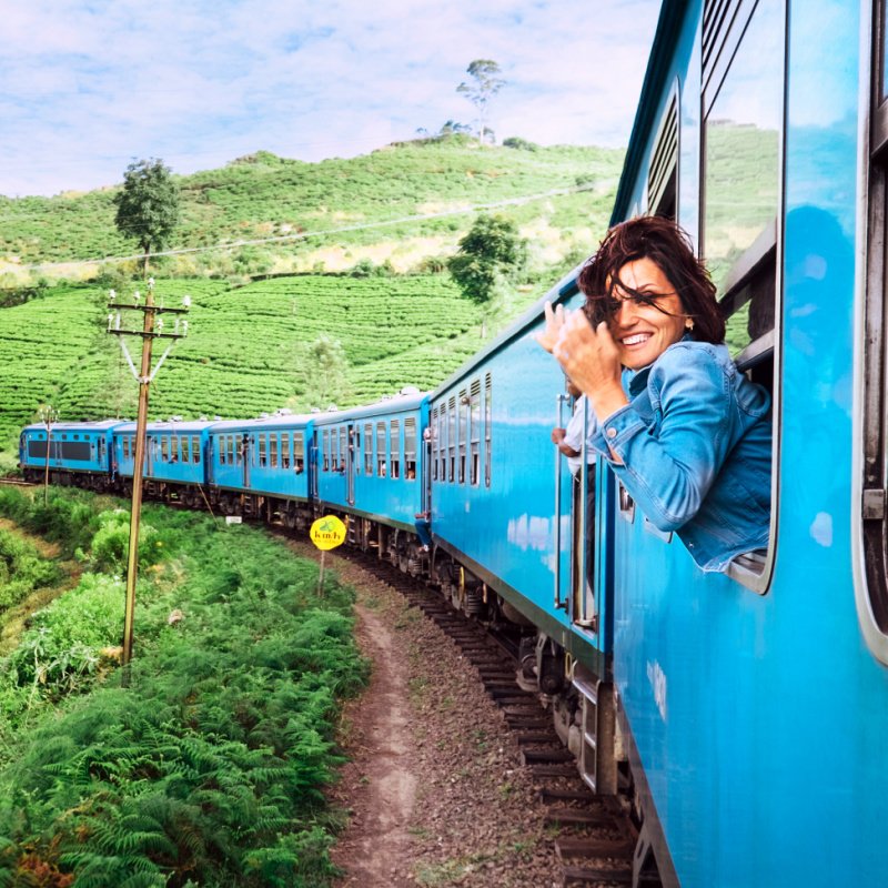 Happy smiling woman looks out from window traveling by train on most picturesque train road in Sri Lanka.