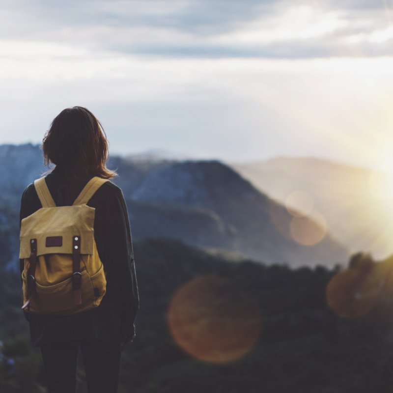 Hipster young girl with backpack enjoying sunset on peak of foggy mountain. Tourist traveler on background view mockup. Hiker looking sunlight in trip in Spain country.