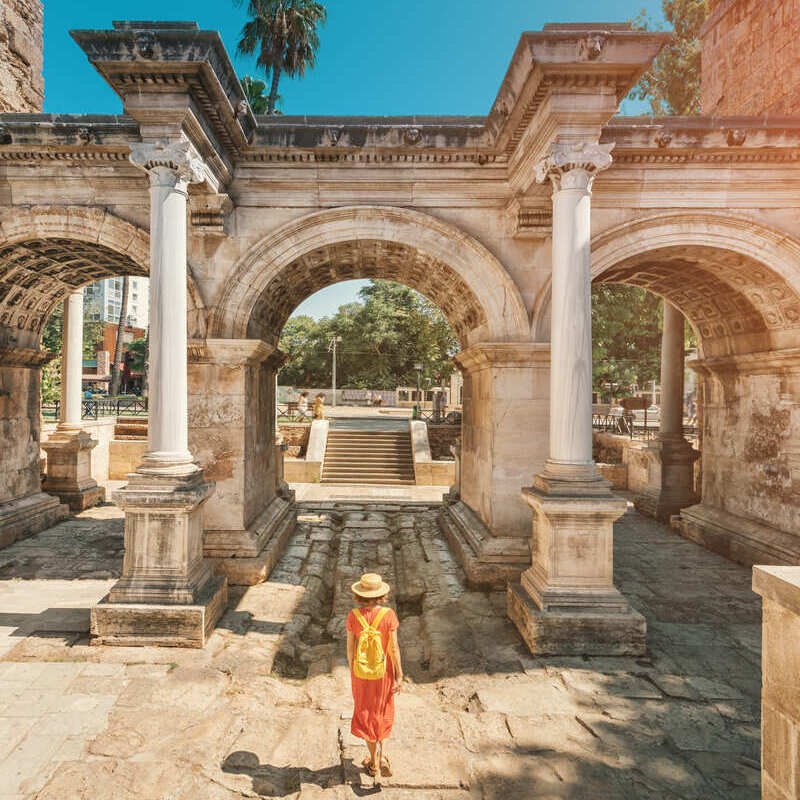 Young Female Tourist Crossing Hadrian's Gate In Kaleici, Old Town Antalya, Turkey