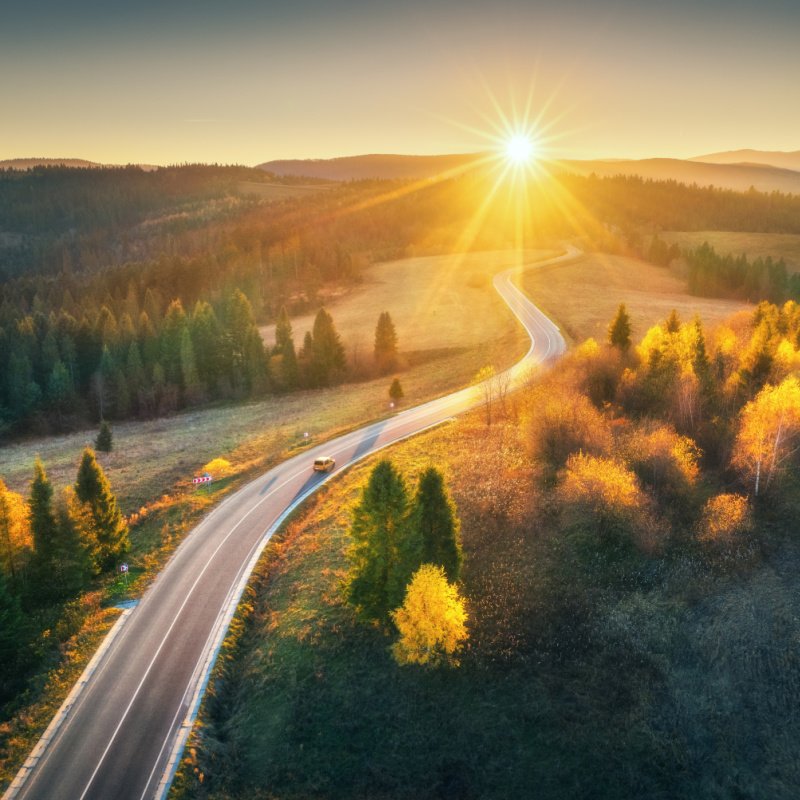 car in the sunset on winding road in fields 