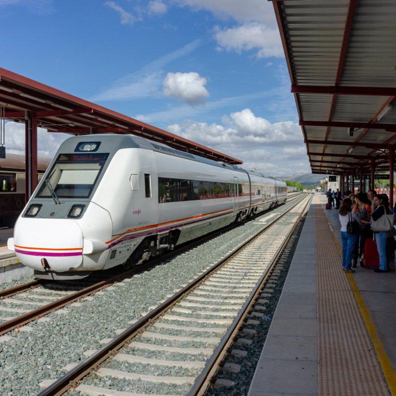 Train pulling into a station with people waiting on the platform