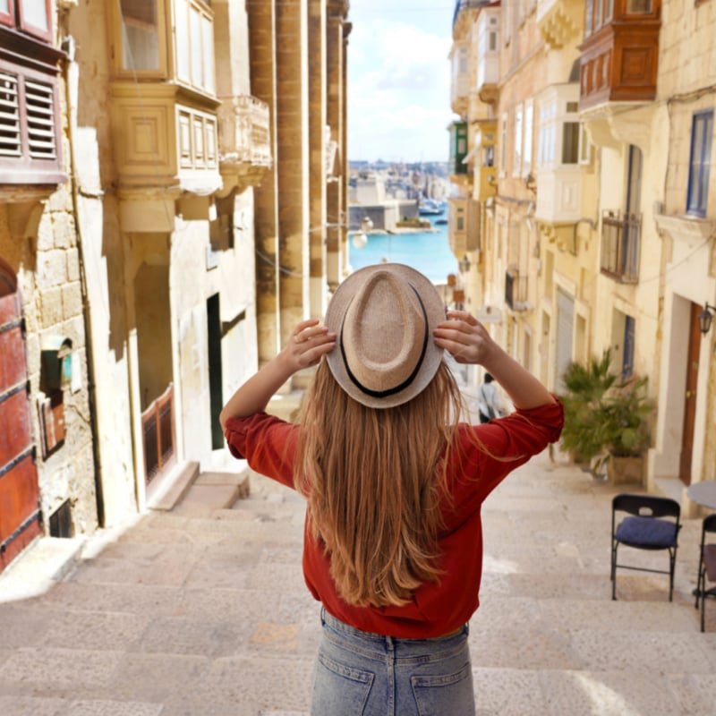 Tourism in Malta. Back view of tourist girl holding hat descends stairs in the old town of Valletta, UNESCO World Heritage, Malta.