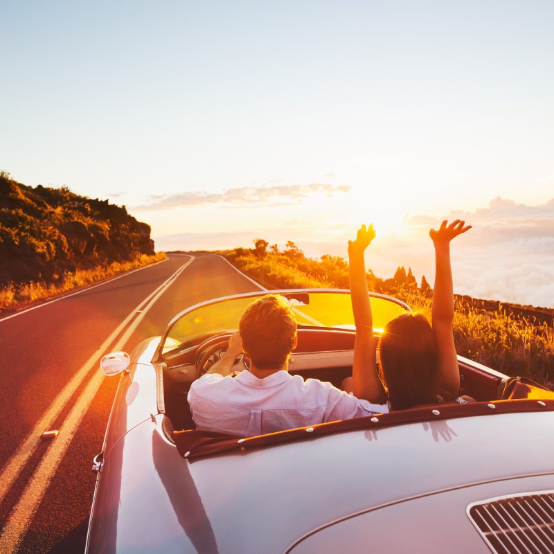 Happy Couple Driving on Country Road into the Sunset in Classic Vintage Sports Car 