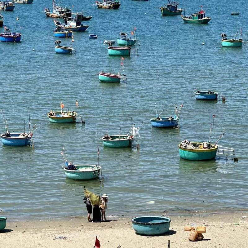 Fishermen Walking The Beach Bounded By The East Sea Filled With Basket Boats, Southern Vietnam, Southeast Asia