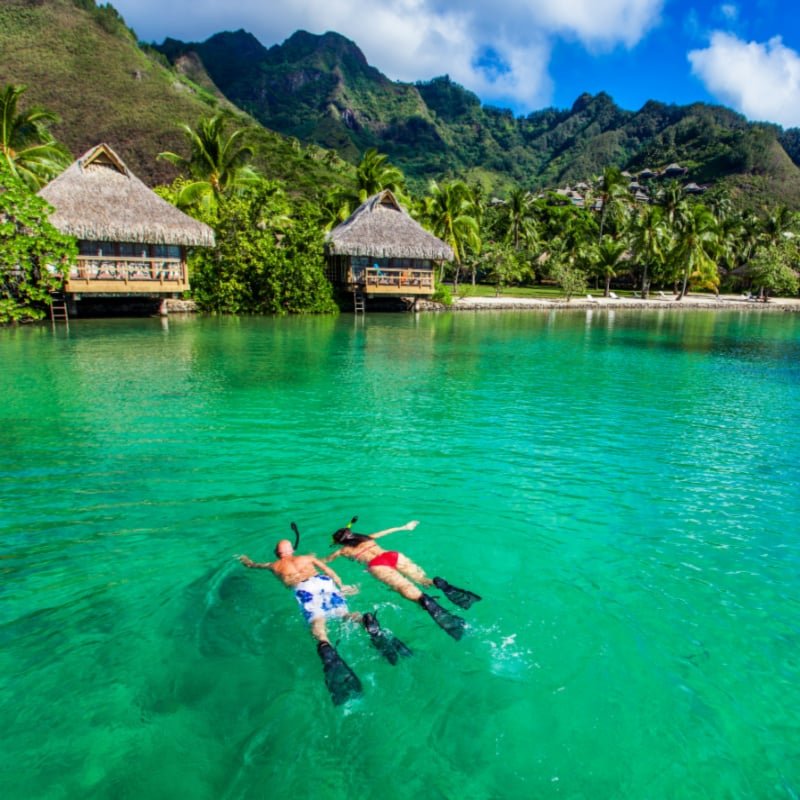 Young couple snorkeling over reef next to resort on a tropical island with over-water villas