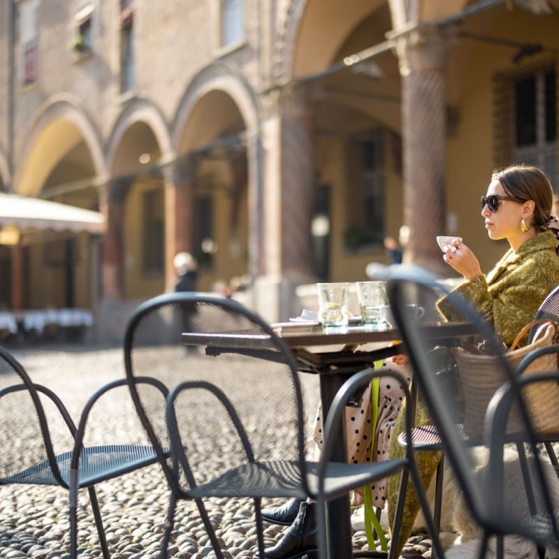 A woman drinking coffee in an outside square in Bologna Italy