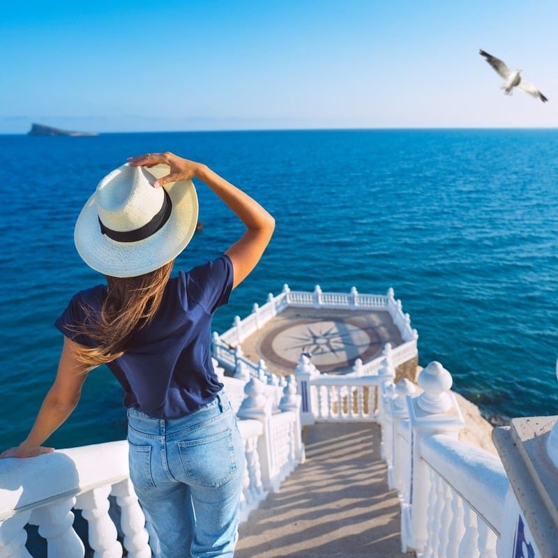 Young Woman Descending A Pretty Staircase Leading Down To The Ocean As A Seagull Flies Overhead, Benidorm, Spain