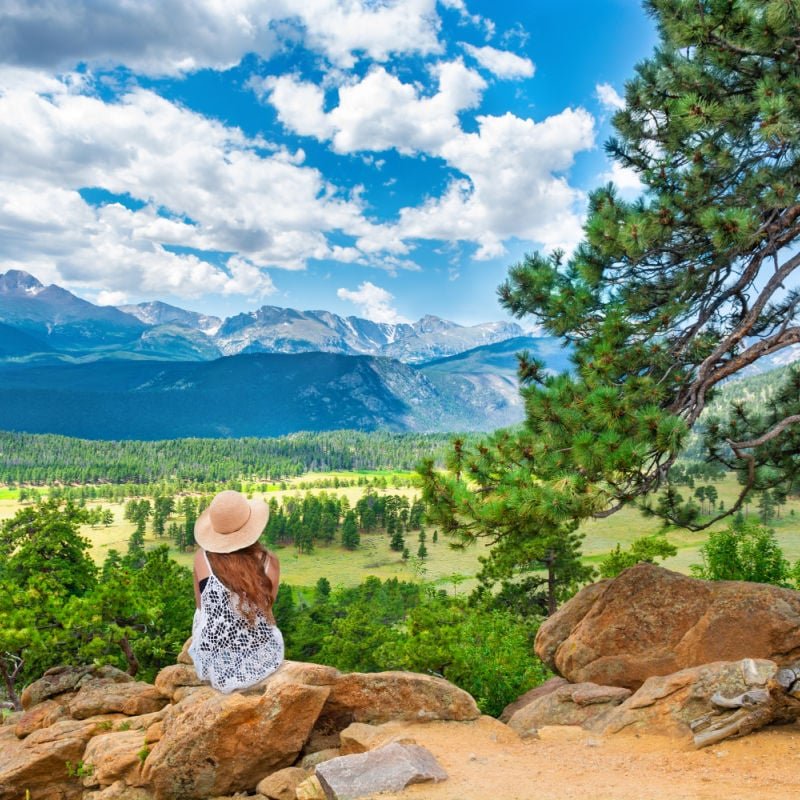 Woman sitting looking at summer mountain view. Rocky Mountain National Park, Estes Park, Colorado, USA.