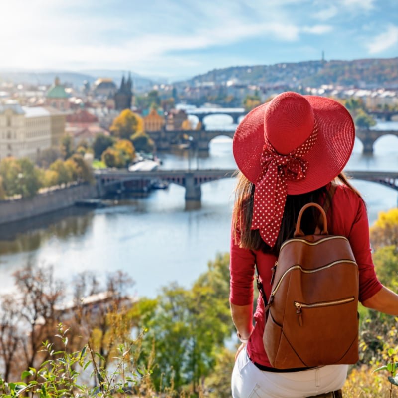 A traveler woman with red hat enjoys the elevated view over the city of Prague, Czech Republic, on a sunny autumn day copy