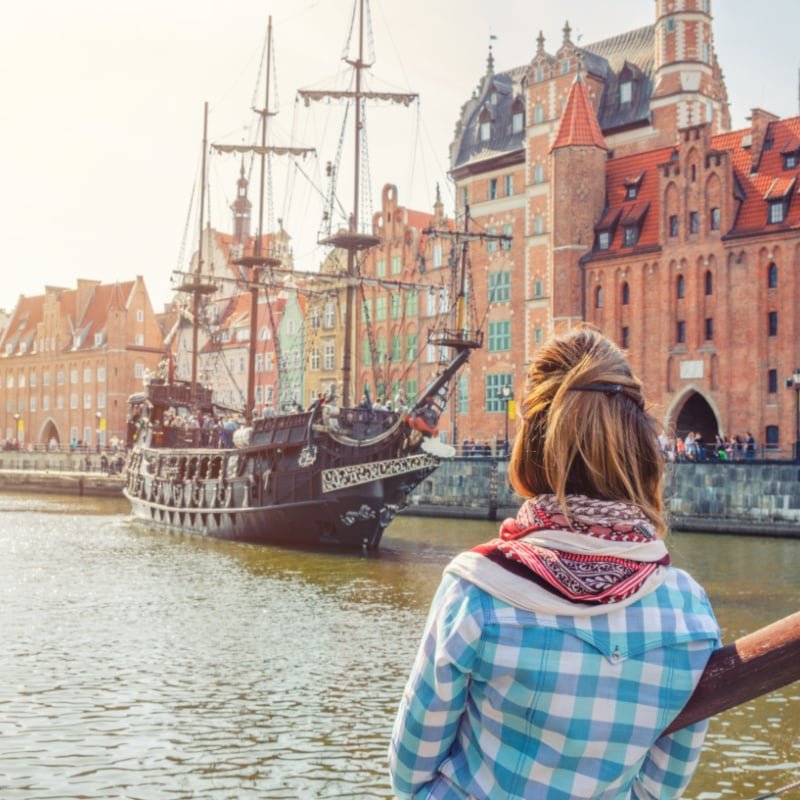 medieval wooden ship and embankment of Motlawa river with old buildings houses in Gdansk city historical centre, view from back