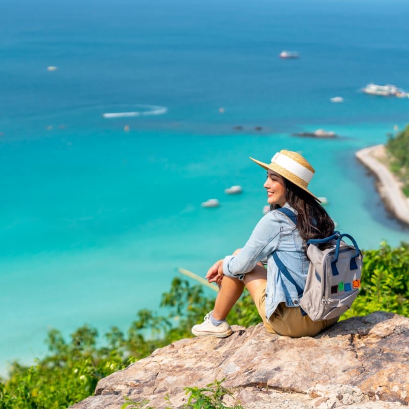 Solo female traveler with backpack looking out over the blue ocean