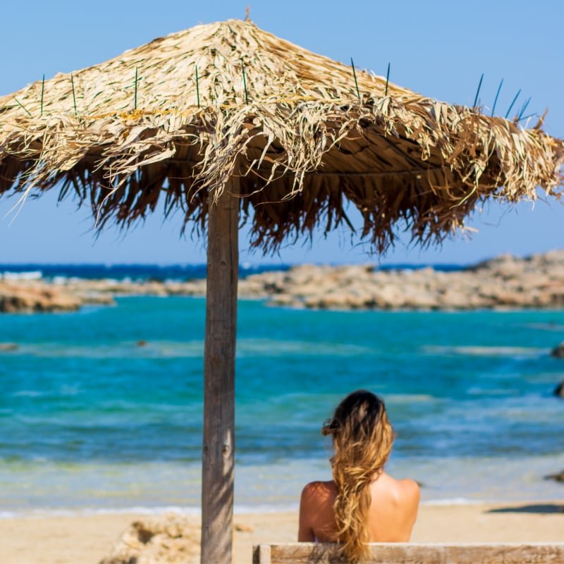 woman under straw umbrella looking at ocean