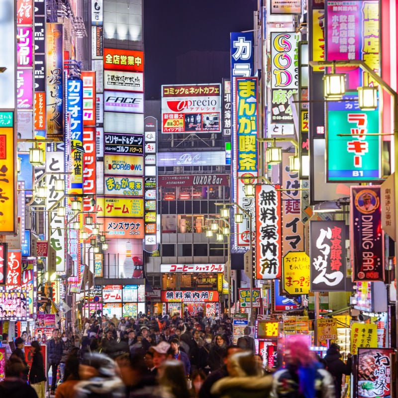 A busy street in Tokyo is lit up by many bright signs