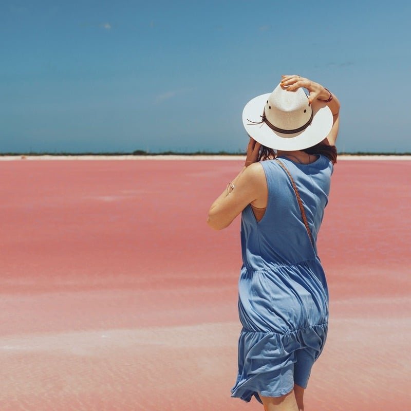 Female Tourist Wearing A Summery Blue Dress And A Straw Hat As She Poses For A Picture By The Las Coloradas Pink Colored Lake, Near Rio Lagartos, State Of Yucatan, Mexico