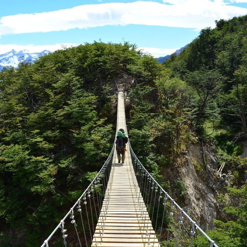 A Backpacker Crossing A Suspended Bridge In Chile, Latin America