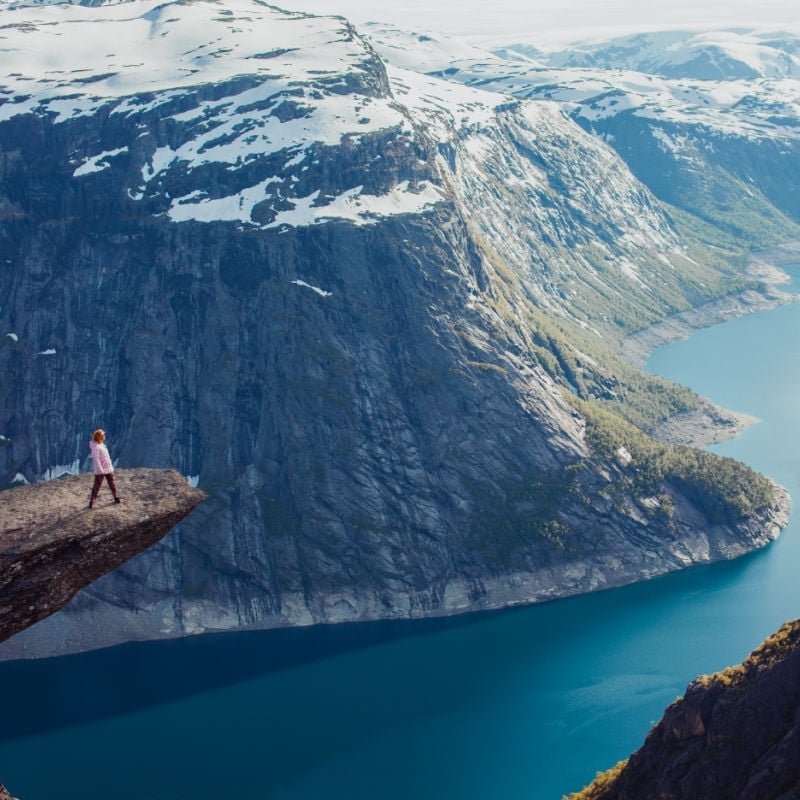 young red girl sneakers stands on a rock and watching the sunset and the mountains, overnight in tent a trip to the mountains, the language of the Troll, Norway fjords, cold weather copy