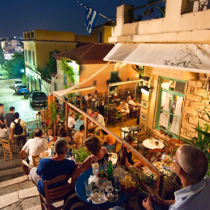 Street with various restaurants and bars, locals and tourists enjoy their meal at night on Plaka area,